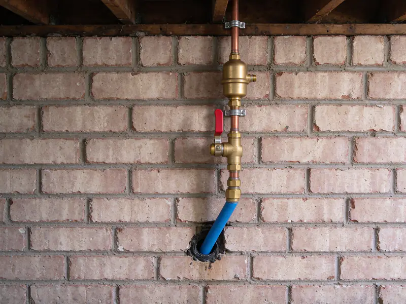 New water service line rising through a crawl space wall to a brass ball valve and pressure-reducing valve
